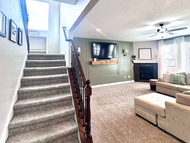Carpeted staircase with wood-finish handrail, recessed lighting, and a living area featuring a fireplace with a dark tile surround