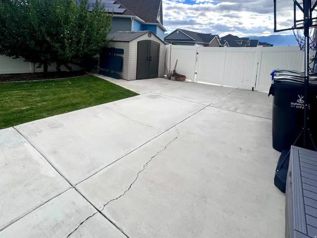 Concrete patio with integrated green space, white privacy fencing, and a detached storage shed