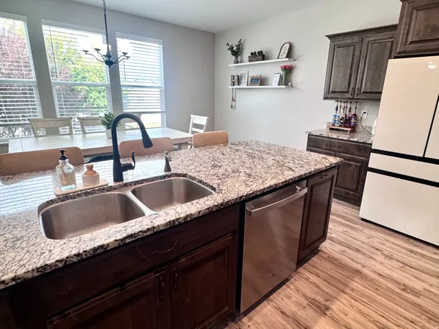 Kitchen island with a double basin sink, granite countertop, dark wood-finish cabinetry, and stainless steel dishwasher