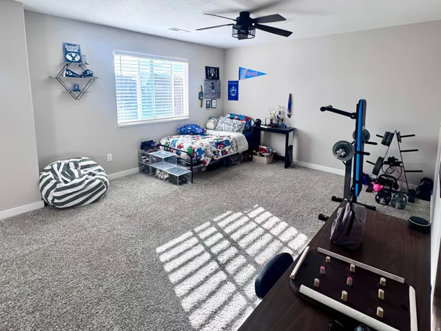 Spacious room featuring neutral carpeting, a ceiling fan, and a large window with blinds