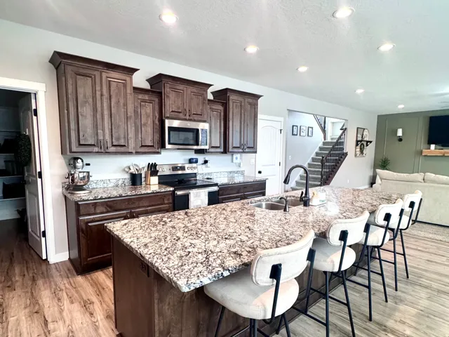 Open-concept kitchen featuring wood-finish flooring, recessed lighting, dark wood cabinetry, and a large central island with seating and a built-in sink