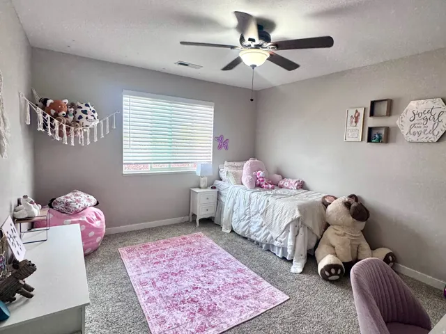 Carpeted flooring, window with horizontal blinds, overhead ceiling fan with lighting, white nightstand, and built-in shelving