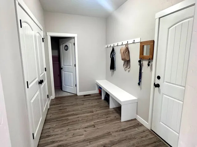 Wood-finish flooring, built-in storage bench, and white paneled doors with black hardware