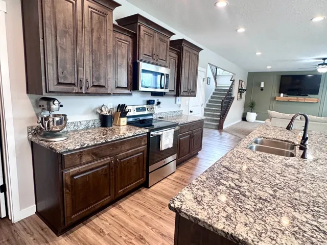 Dark wood-finish cabinetry, stainless steel appliances, speckled stone countertops, wood-finish flooring, and recessed lighting throughout