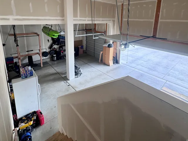 Spacious garage with unfinished drywall, exposed wood-finish stairs, and concrete flooring