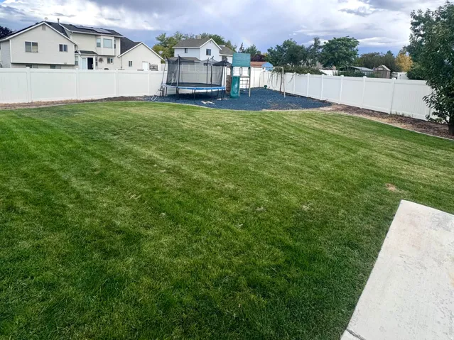 Expansive backyard featuring a green lawn, white vinyl fencing, and a concrete patio