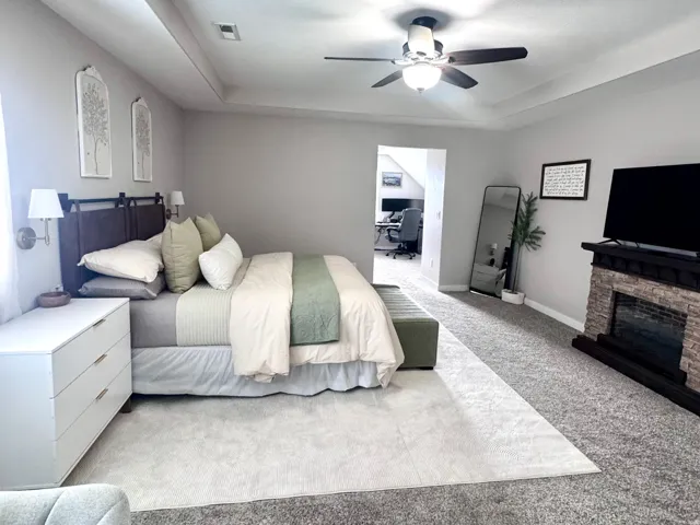 Tray ceiling, recessed lighting, ceiling fan, stone-finish fireplace, and neutral carpeting
