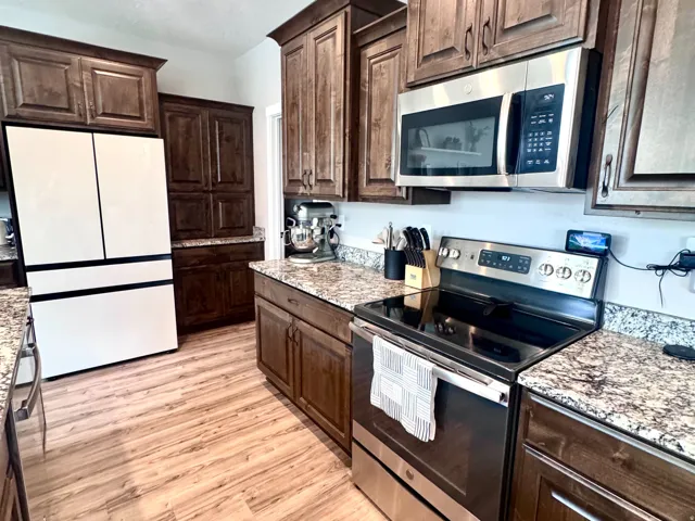 Wood-finish flooring, dark wood cabinetry, granite countertops, and stainless steel appliances