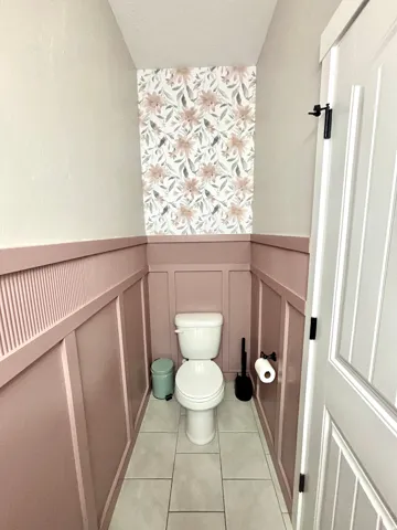 Powder room featuring board and batten wainscoting, floral accent wallpaper, and light-toned floor tiling