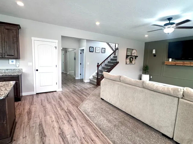 Wood-finish flooring, recessed lighting, ceiling fan, dark wood cabinetry, and a carpeted area