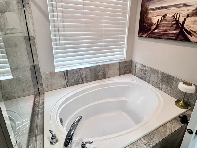 Built-in soaking tub with chrome fixtures, surrounded by gray-toned tiled walls and a white surface