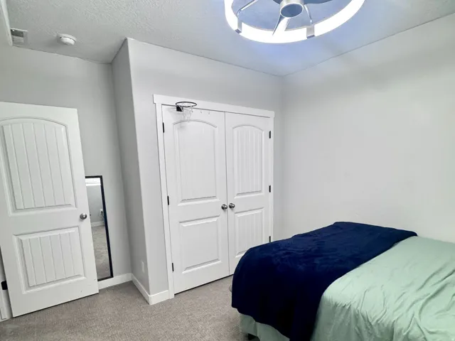 Textured gray carpeting, contemporary ceiling fan with integrated lighting, white paneled doors, and a double-door closet