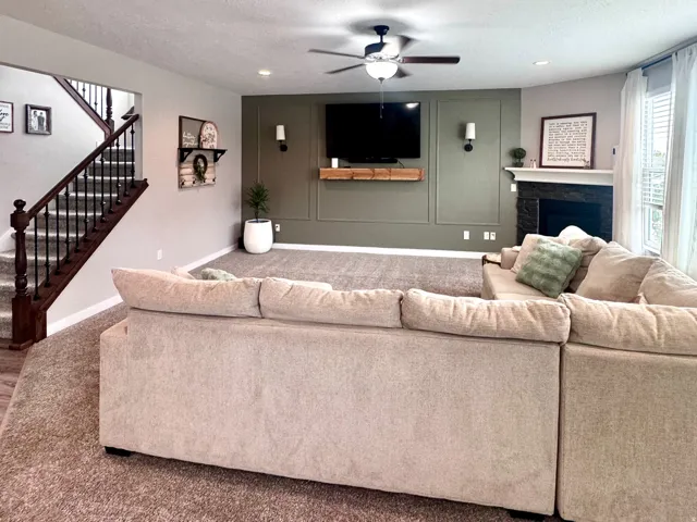 Recessed lighting, ceiling fan, fireplace with mantel, decorative wall paneling, and a staircase with dark wood handrails