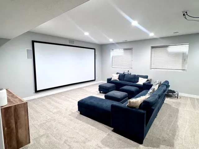 Integrated projection screen, recessed ceiling lighting, light gray wall finishes, light-toned carpet, and multiple windows with blinds