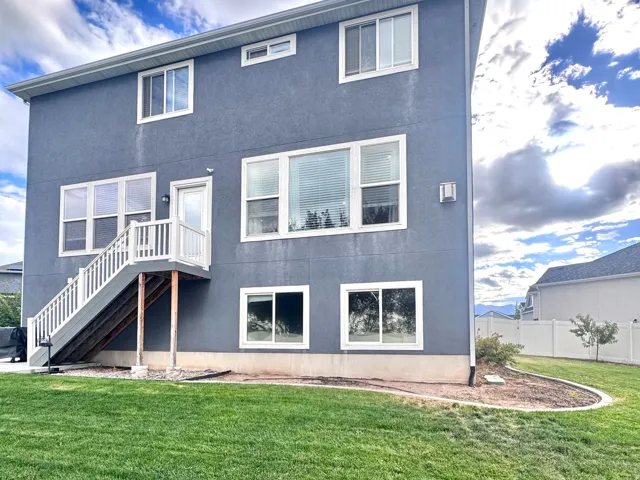 Two-story stucco exterior with multiple large windows, a raised deck with white railings, and an expansive lawn