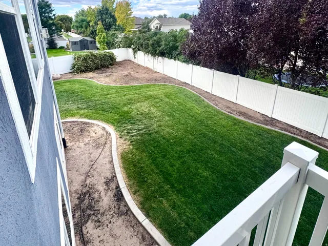Private backyard with manicured lawn, white vinyl fencing, and mature trees
