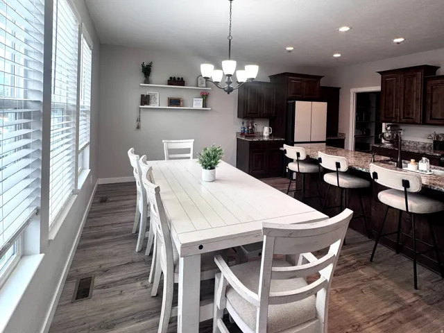 Open-concept dining area with wood-finish flooring, a contemporary chandelier, and multiple windows