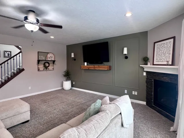 Carpeted living area featuring a ceiling fan, recessed lighting, and a fireplace with a dark stone surround and white mantle