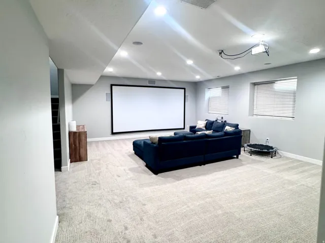 Spacious room featuring a projector screen, recessed lighting, carpet flooring, and multiple windows