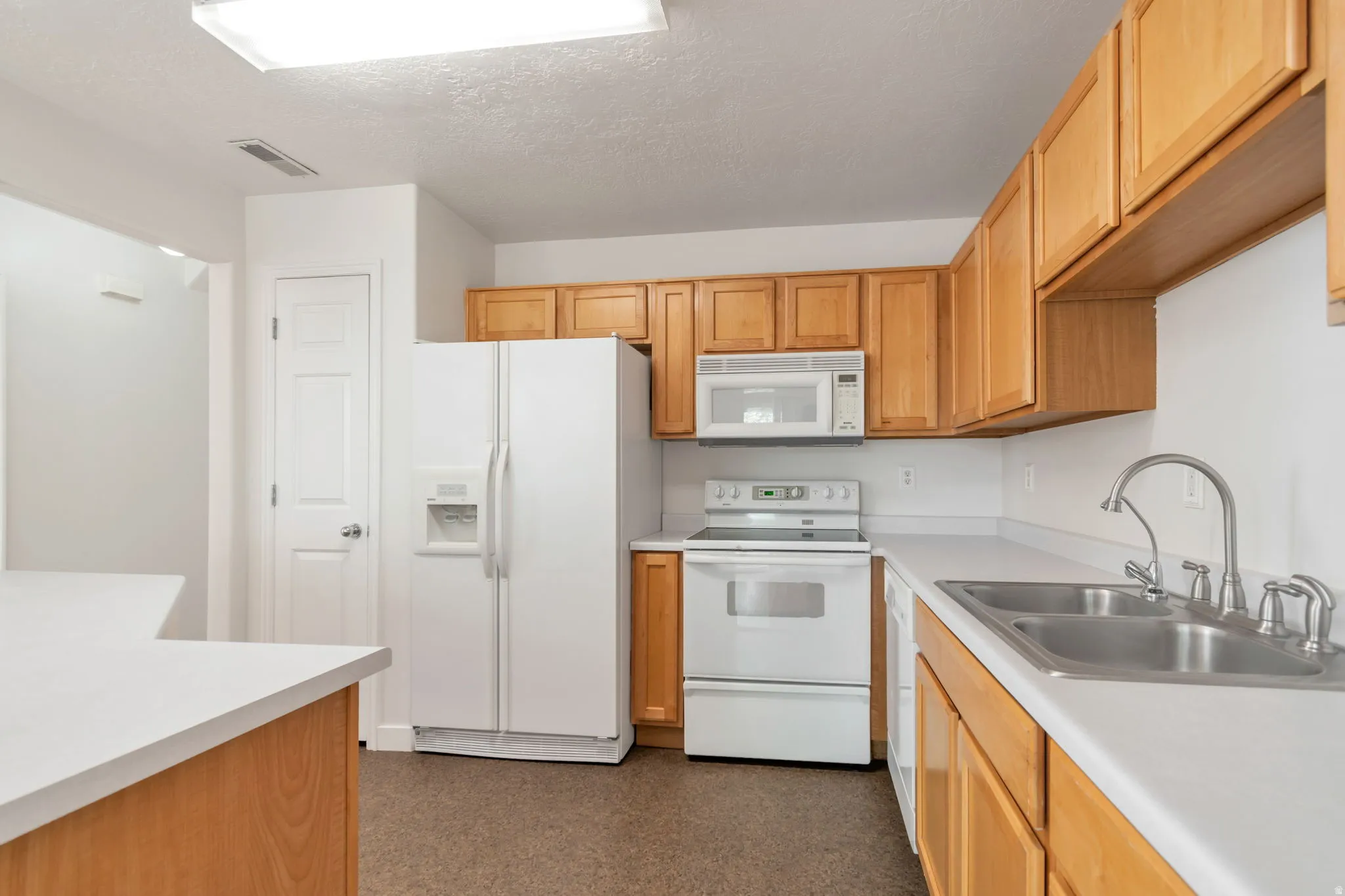 Kitchen featuring wood cabinetry, white countertops, dual basin stainless steel sink, and white appliances