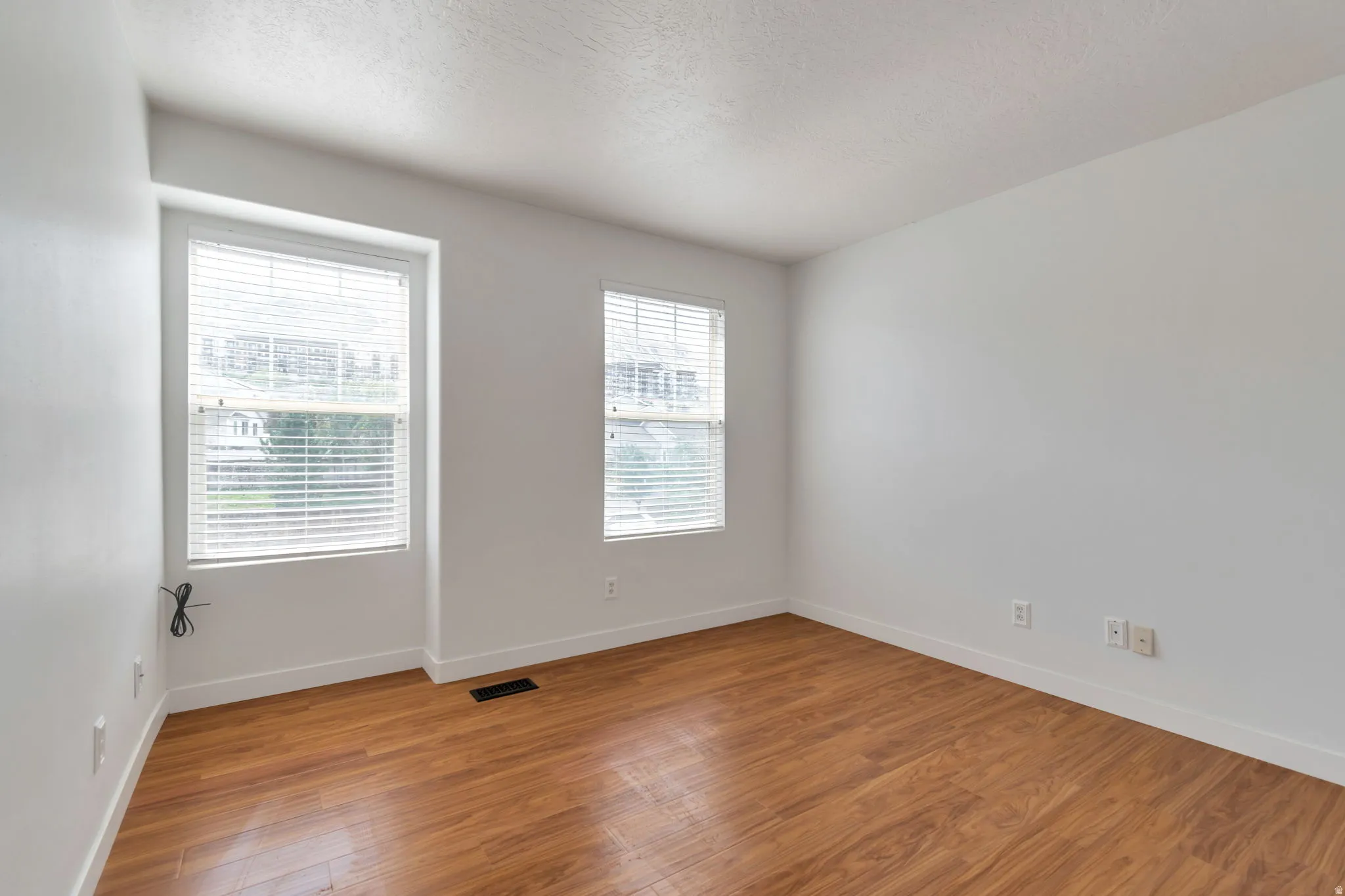 Bright room featuring wood-finish flooring and two double-hung windows with blinds