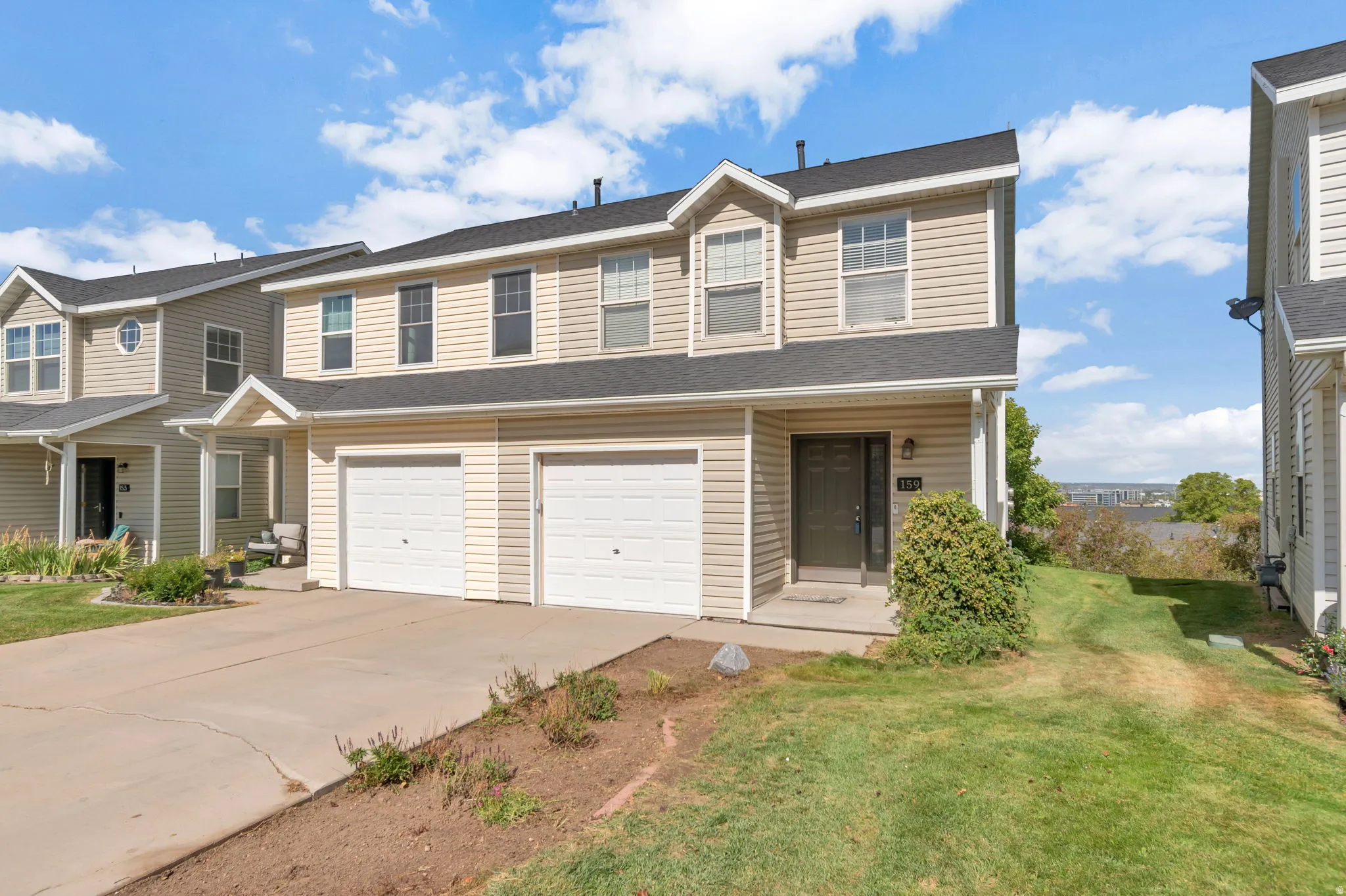 Two-story residence featuring light-colored siding, a dark roof, two garage doors, a covered entry, and a paved driveway
