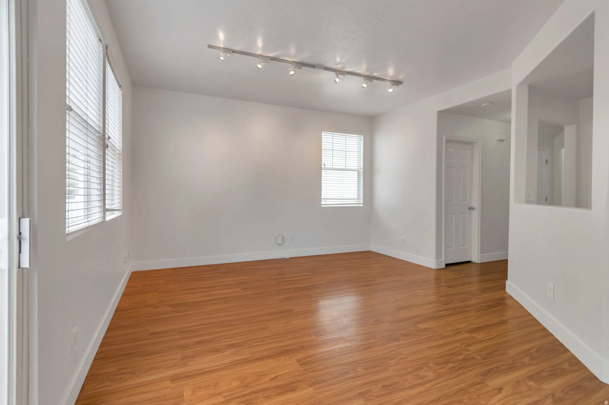 Wood-finish flooring throughout, multiple windows with blinds, recessed wall niche, and track lighting fixture