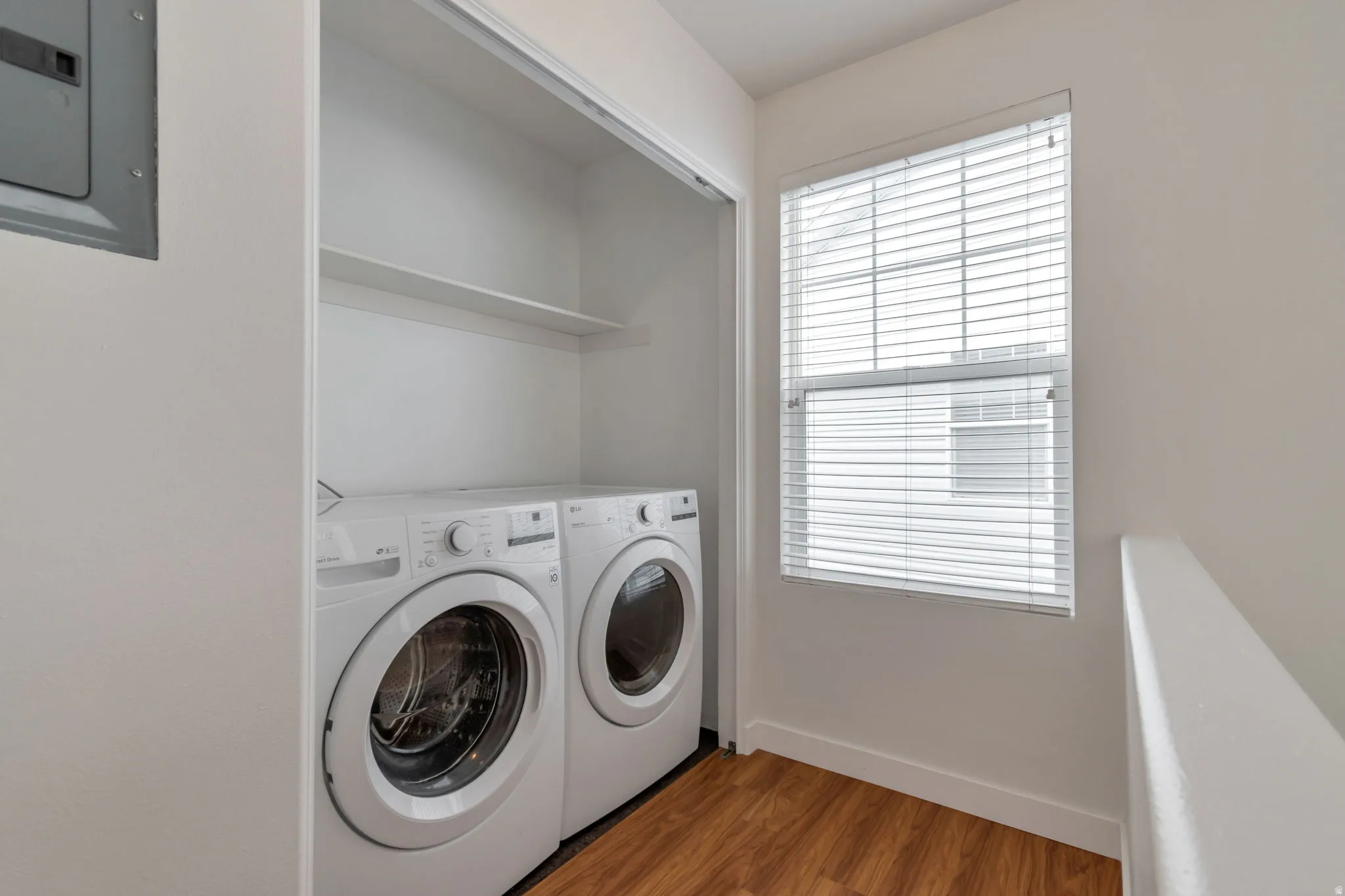 In-unit laundry area with wood-finish flooring, a window, and shelving