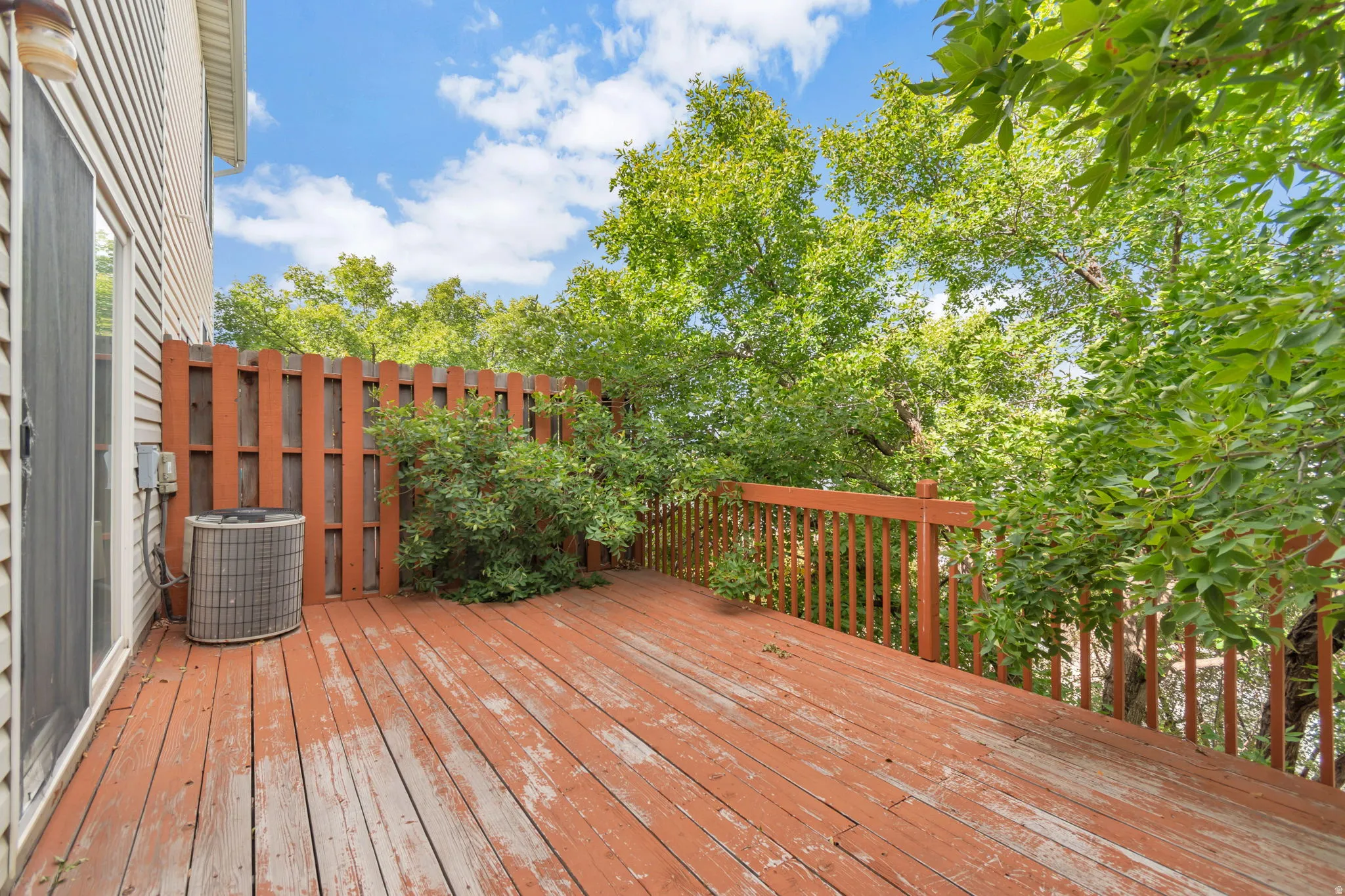 Expansive outdoor deck with wood railing, privacy fence, and mature foliage