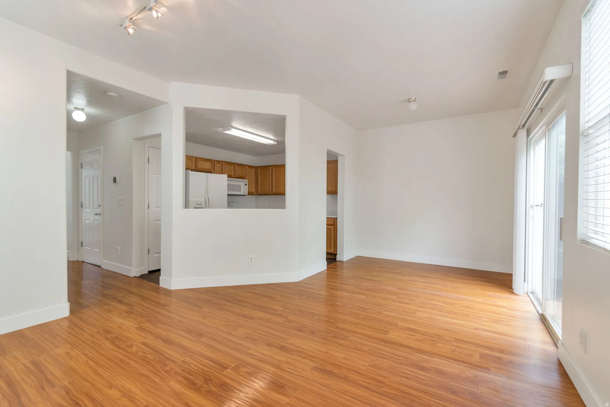 Warm wood-finish flooring throughout, a kitchen pass-through window, and sliding glass doors with vertical blinds