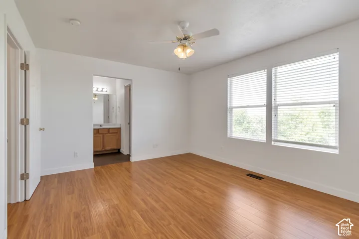 Spacious room featuring wood-finish flooring, two large windows with blinds, and a ceiling fan with integrated lighting