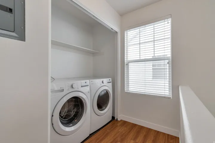 In-unit laundry area with wood-finish flooring, a window, and shelving
