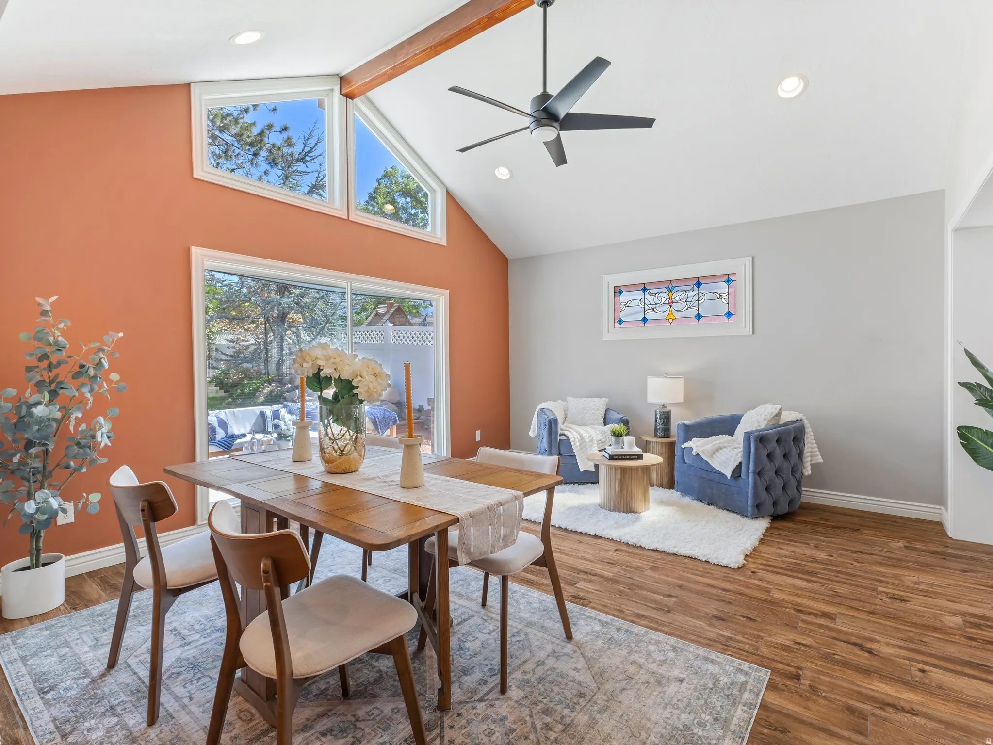 Vaulted ceiling with an exposed wood beam, wood-finish flooring, sliding glass door, triangular accent windows, and recessed lighting