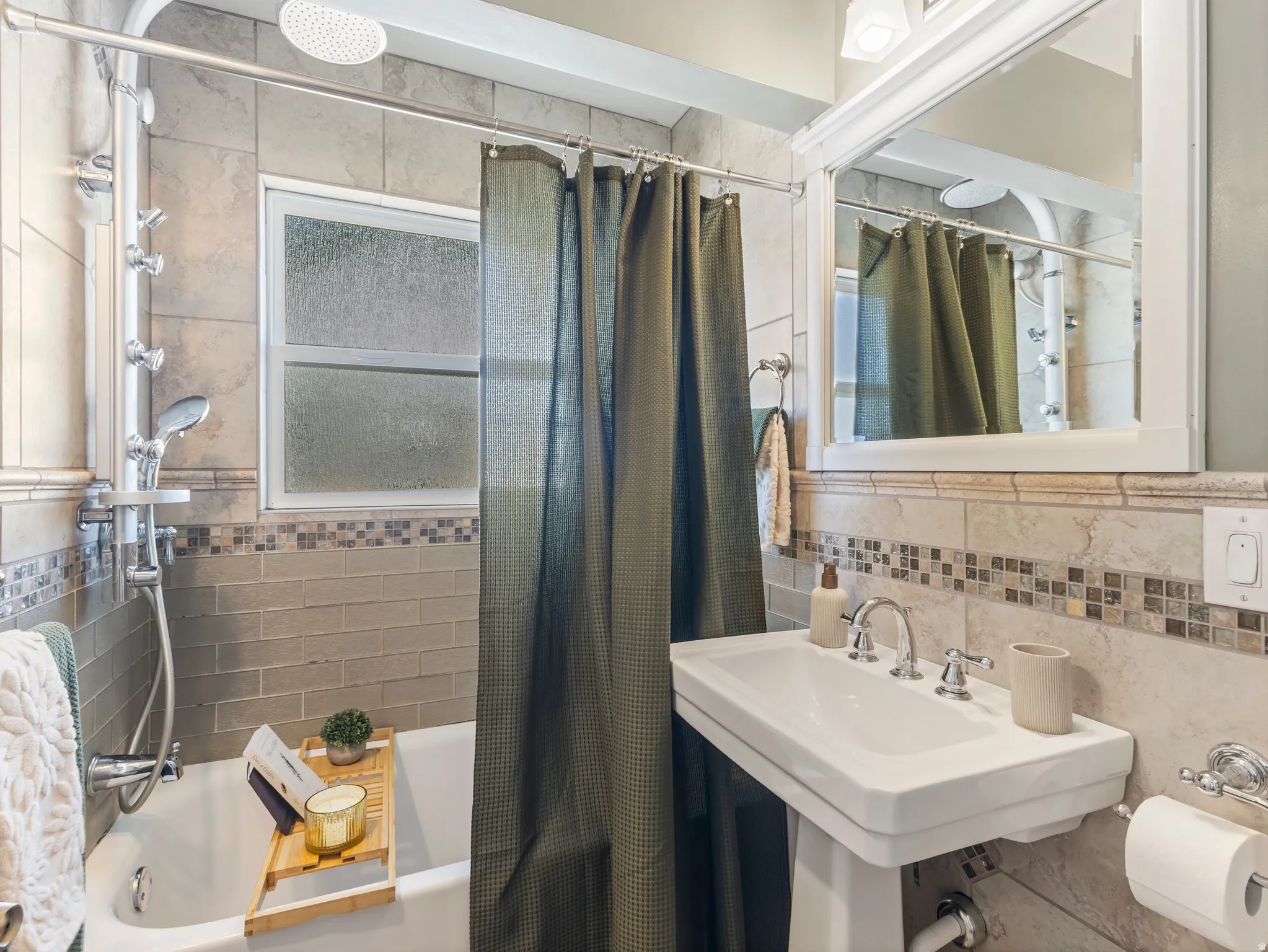 White pedestal sink with chrome fixtures, tiled wall with mosaic accent, white framed mirror, and a window with frosted glass