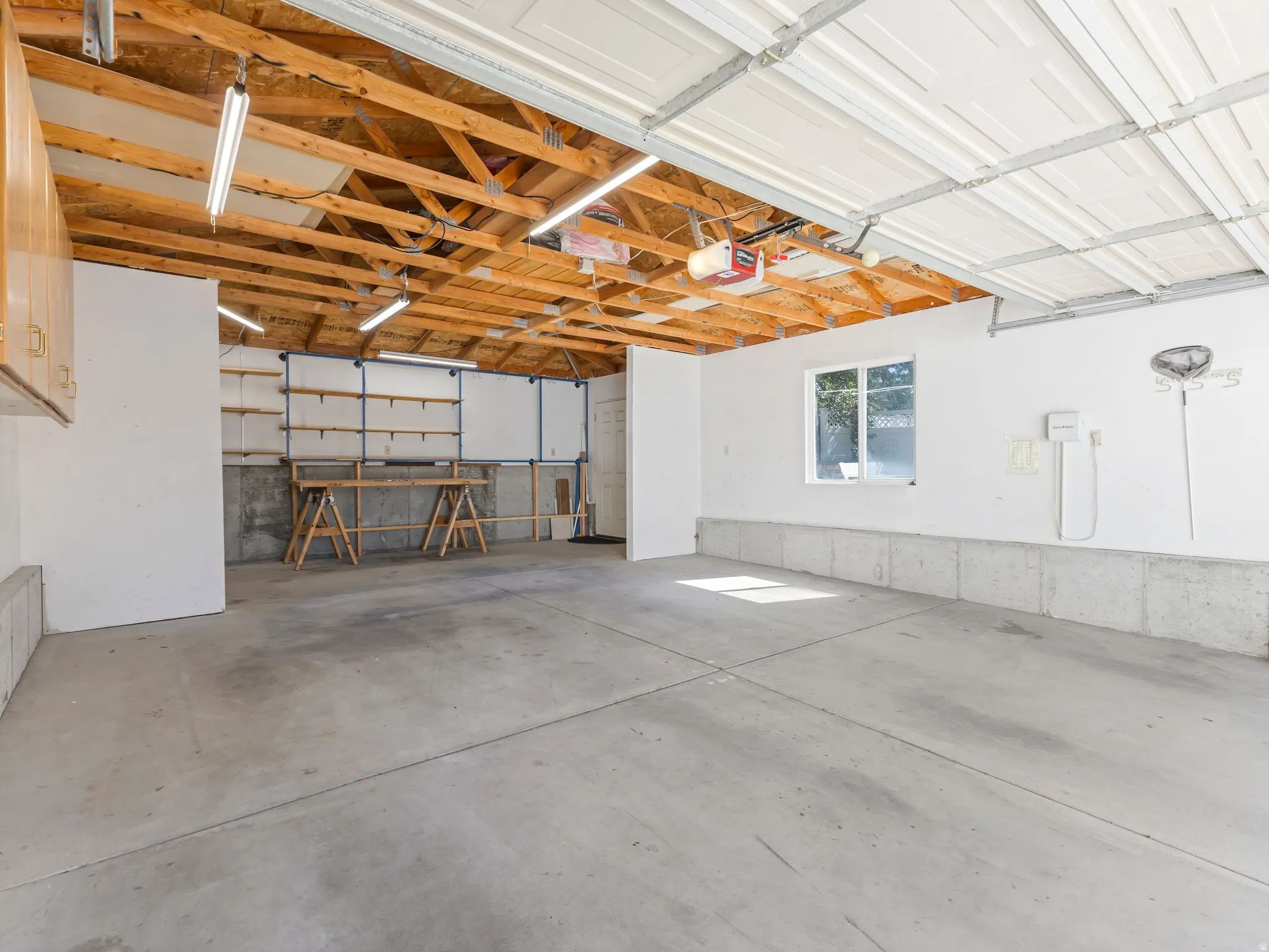 Spacious garage featuring a concrete floor, exposed wood beam ceiling, ample built-in shelving, a large window, and wall-mounted cabinetry