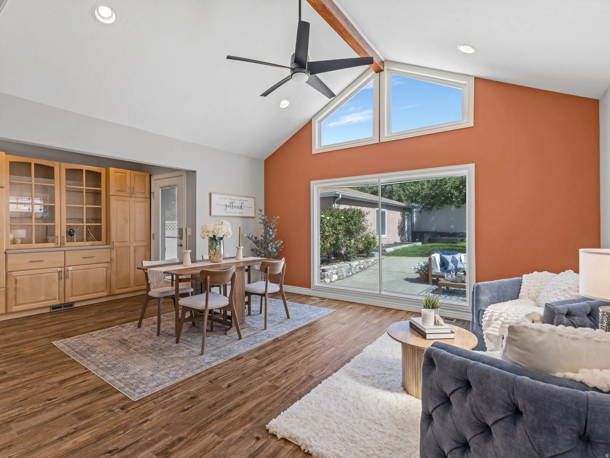 Vaulted ceiling with exposed beam, wood-finish flooring, built-in cabinetry with glass panels, recessed lighting, and expansive sliding glass doors
