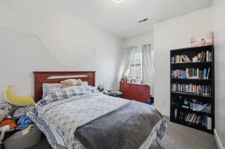 Carpeted room with a window featuring drapes, white walls, and a wooden headboard