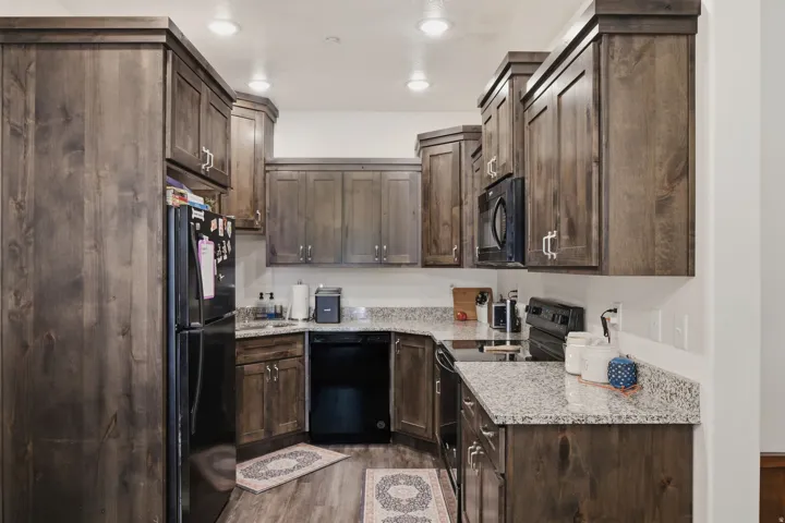 Galley kitchen featuring wood-finish cabinetry, granite countertops, and black appliances