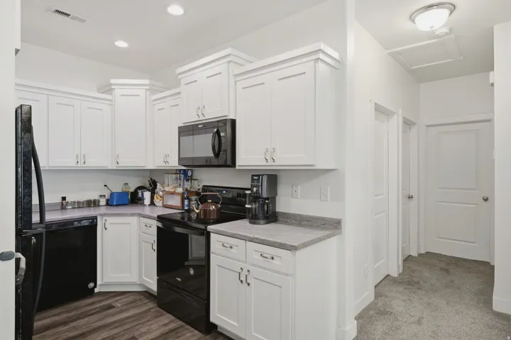 White shaker-style cabinetry with crown molding, black kitchen appliances, granite-finish countertops, wood-finish flooring, and recessed lighting