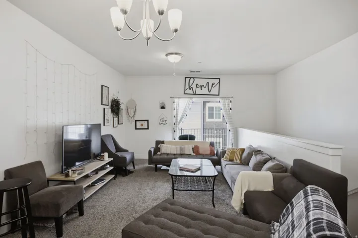 Spacious living area featuring neutral carpeting, a contemporary chandelier, recessed lighting, and a balcony