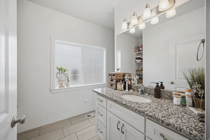 Dual-sink vanity with granite countertop, white cabinetry, and brushed nickel hardware