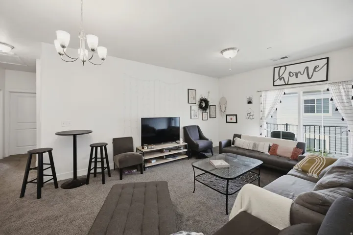 Carpeted living area with white walls, ceiling-mounted lighting, and a sliding glass door to an outdoor balcony