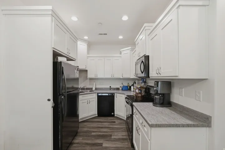 White cabinetry with crown molding, dark wood-finish flooring, recessed lighting, and black appliances