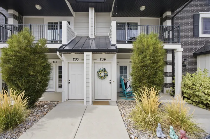 Exterior featuring dark brick accents and light siding, an upper-level balcony with black railings, and a lower-level entrance with a covered porch