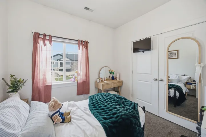 Double-pane window with white trim, white walls, built-in closet doors with round knobs, and gray carpet flooring