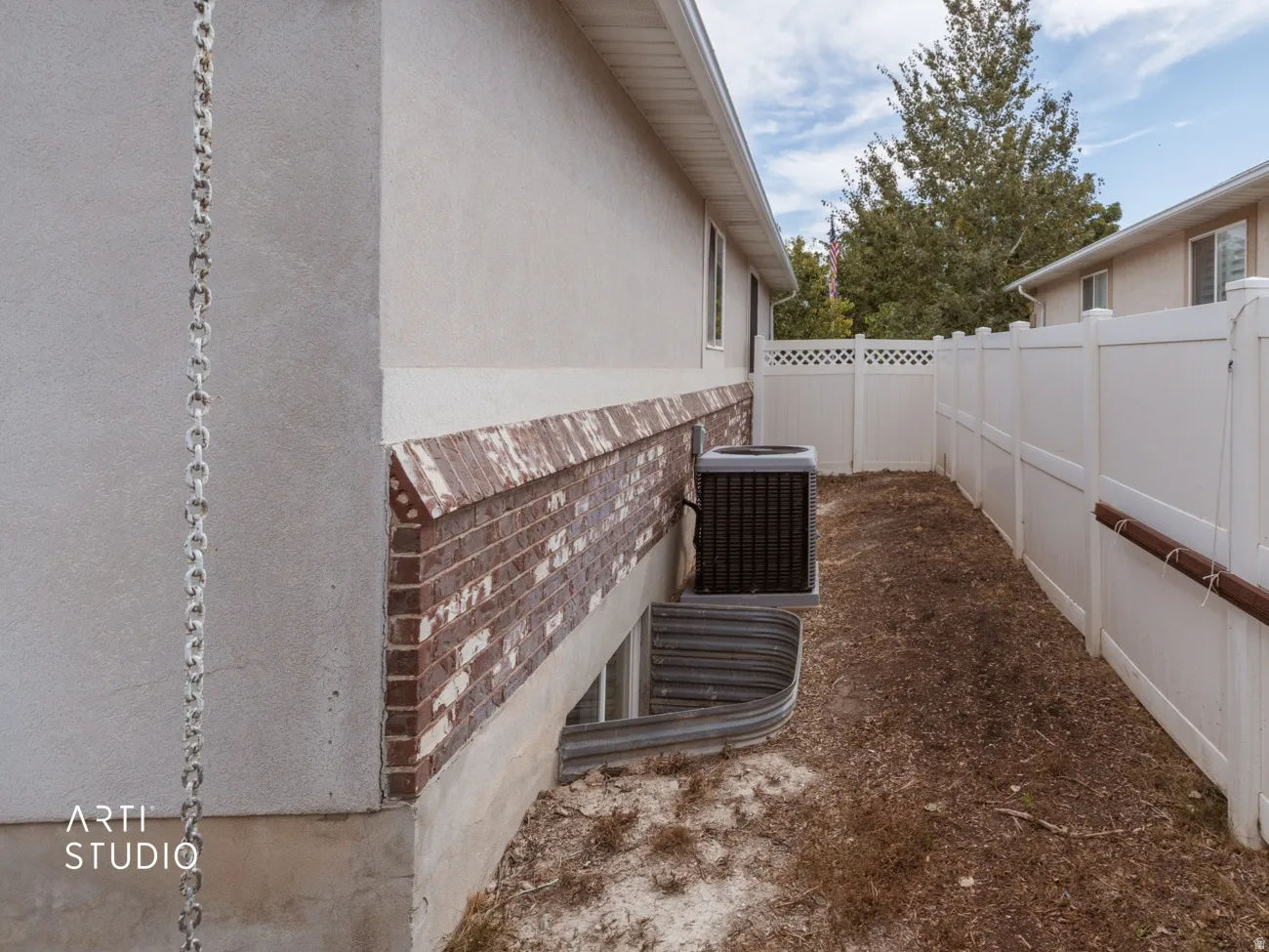 Property exterior featuring stucco siding, brick detailing, a window well, and a white privacy fence