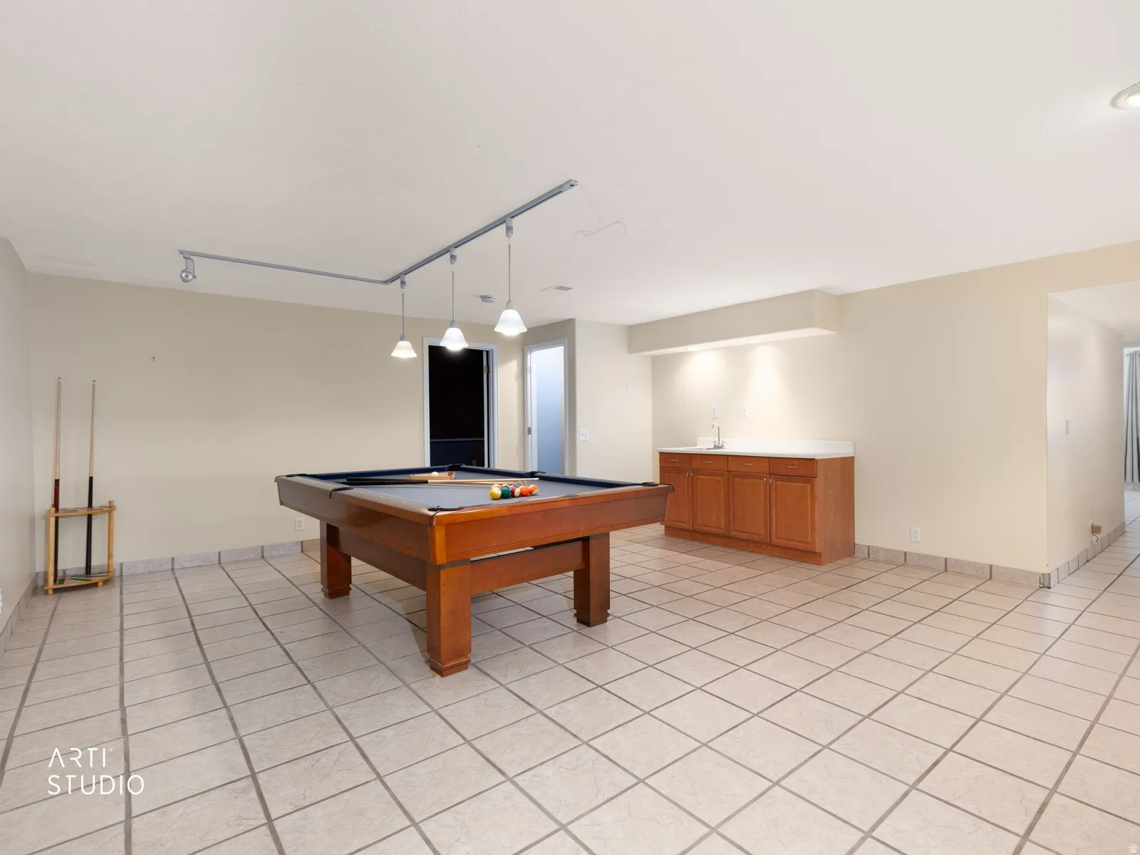 Spacious room with light-toned tile flooring, track lighting, and a built-in wood-finish cabinet with a light-toned countertop