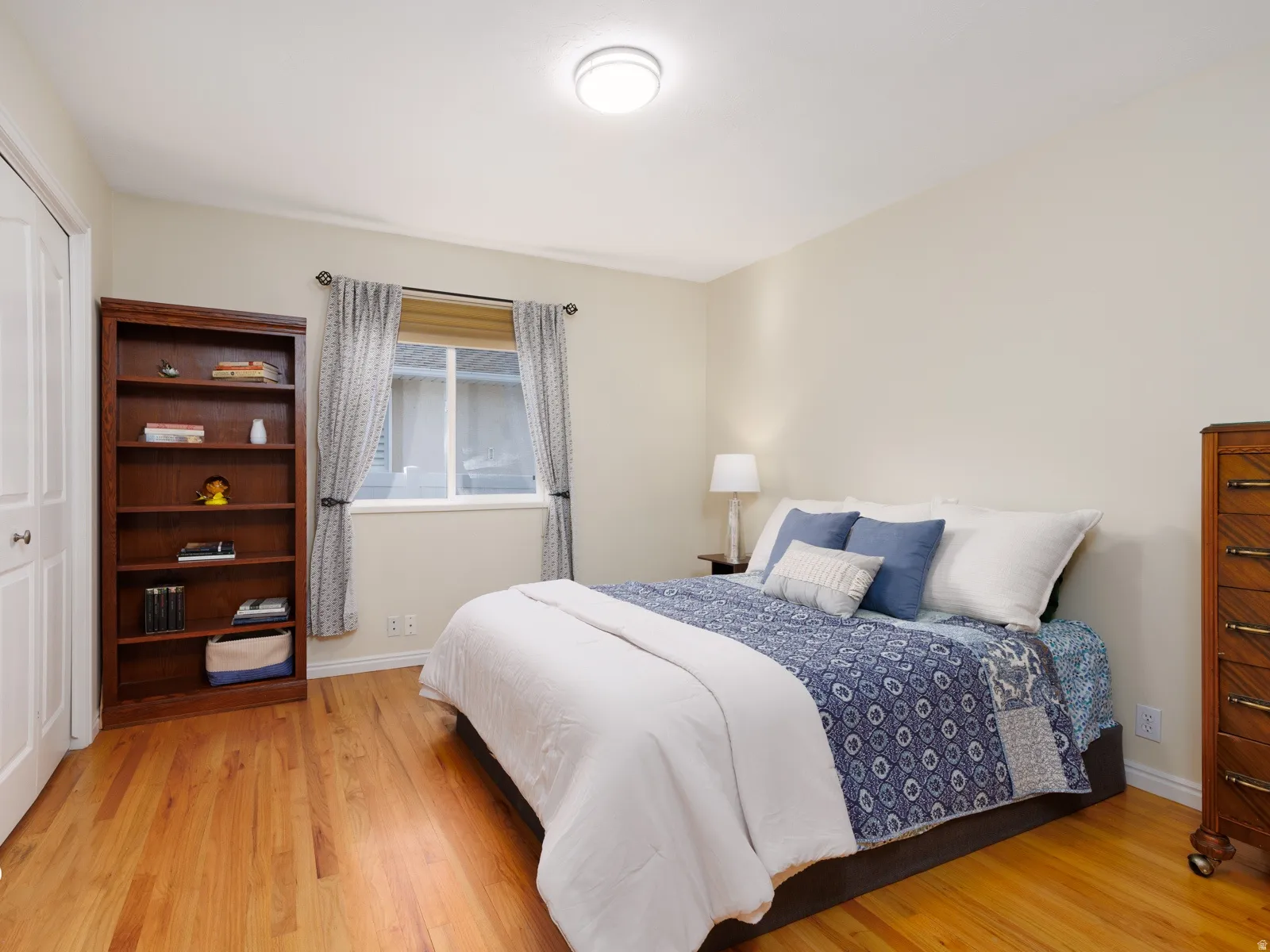 Hardwood flooring, neutral wall tones, window with vertical blinds, ceiling-mounted light fixture, and white bi-fold closet doors