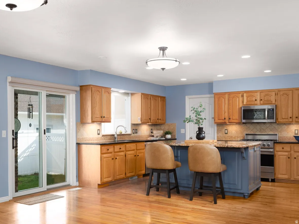 Hardwood flooring throughout, kitchen island with seating, stainless steel appliances, wood cabinetry, and a sliding glass door