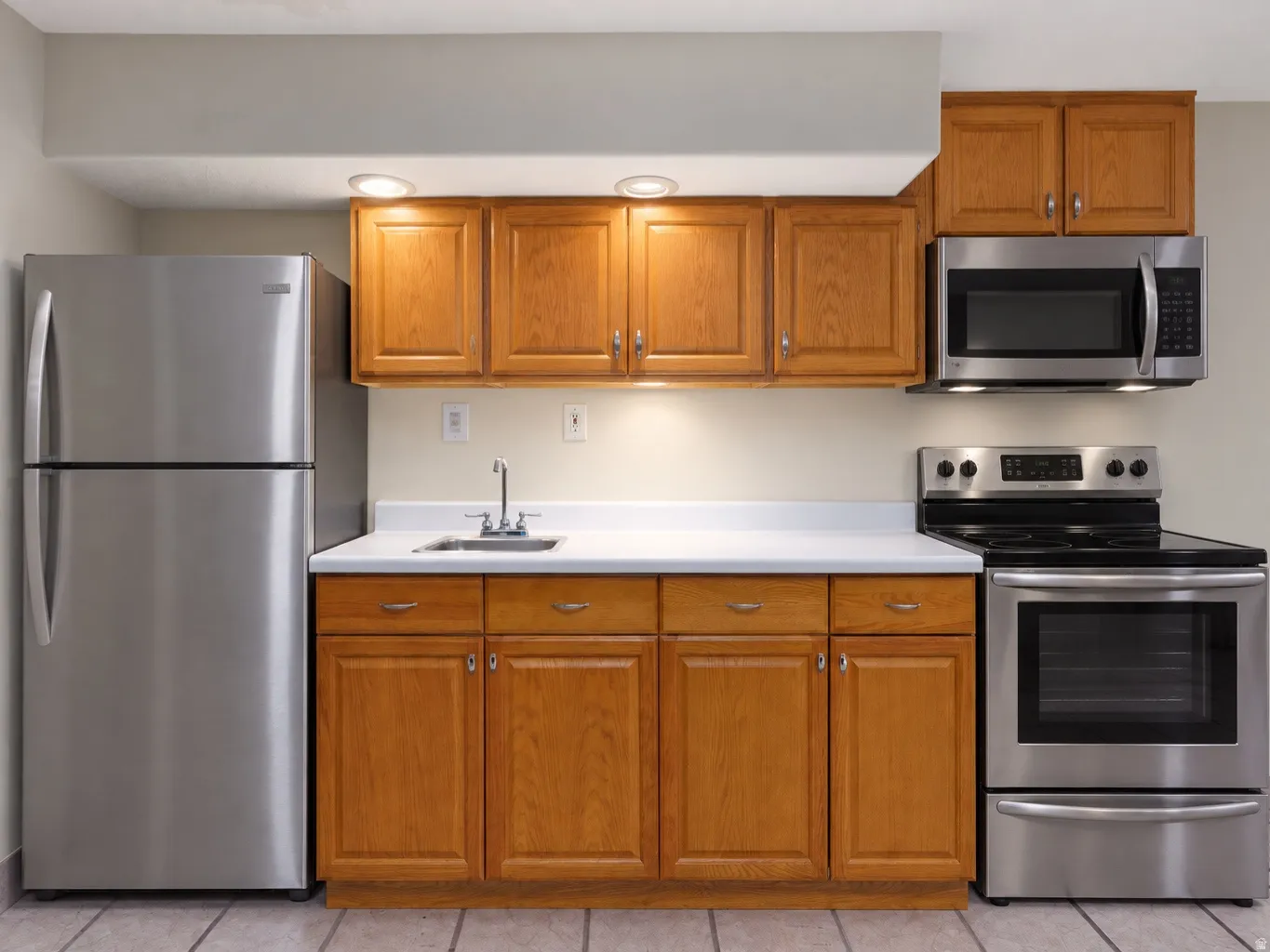 Full kitchen with stainless steel appliances, wood-finish cabinetry, and white countertops digitally staged appliances and upper cabinetry.